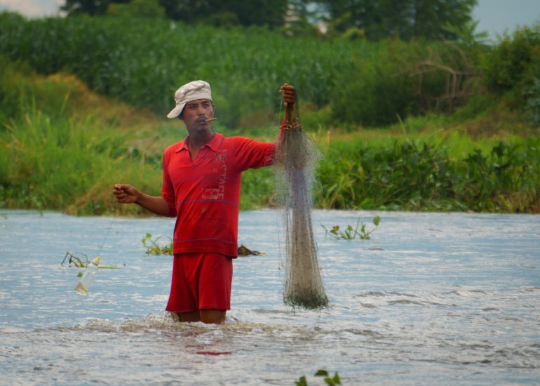 Burmese mit roter Kleidung steht in einem Fluss mit Fischernetz in der Hand