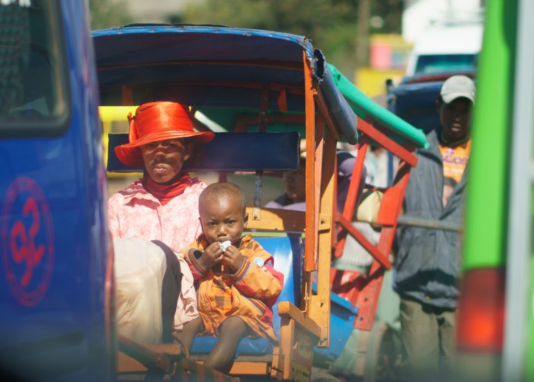 Frau mit rotem Hut und kleinem Kind sitzt auf einer bunten Rikscha