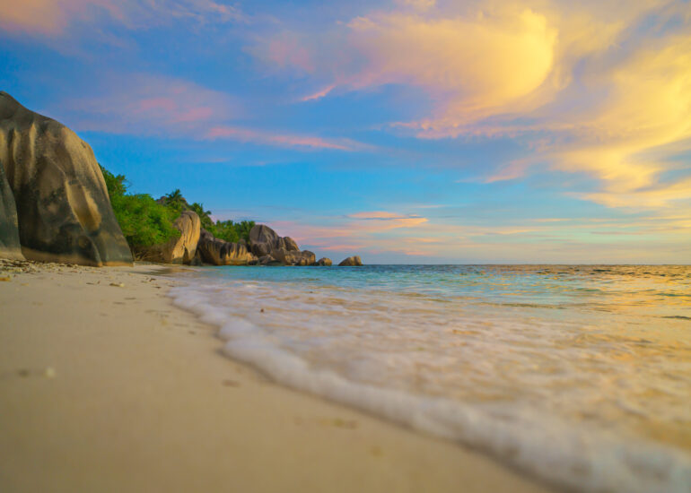 Strandbild mit buntem Himmel durch untergehende Sonne und Welle die Richtung Betrachter fließt